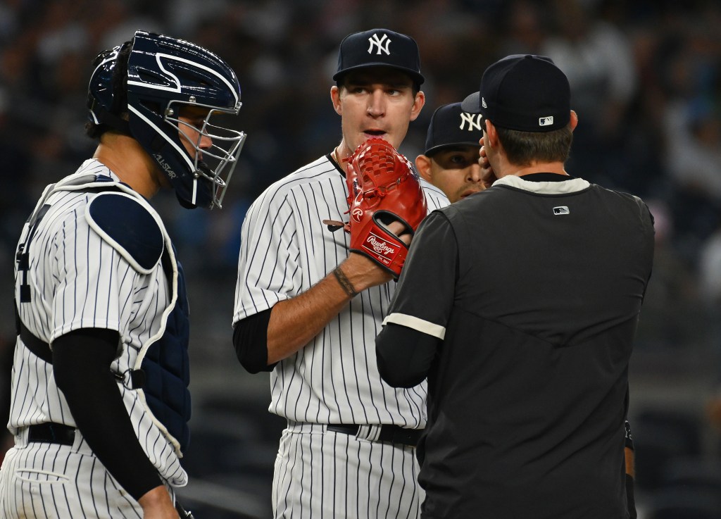 Yankees pitcher Andrew Heaney #38 reacts on the mound after giving up two home runs, with a catcher and coach.