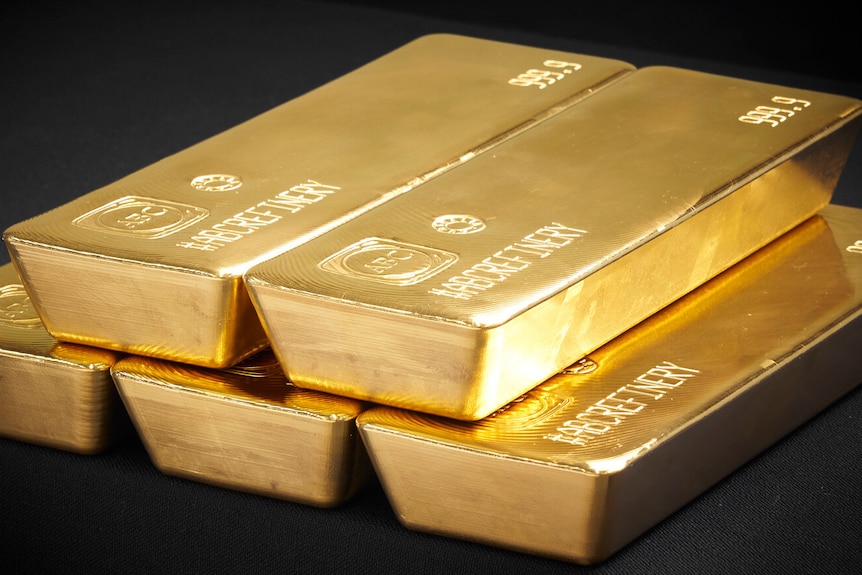 2 gold bars sit on 3 gold bars. Each has engraving on it with 999.9, a logo and an ID number