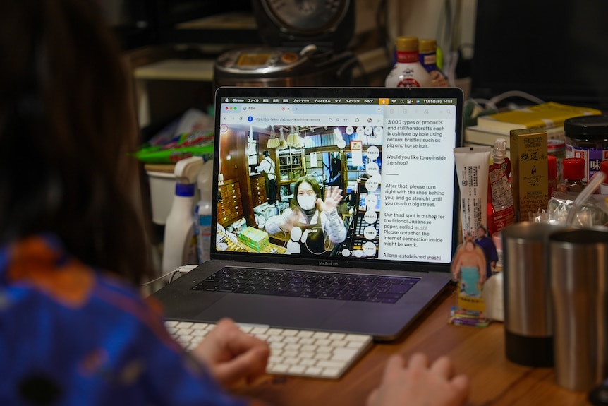 A woman can be seen from behind sitting at a desk working on a laptop. 