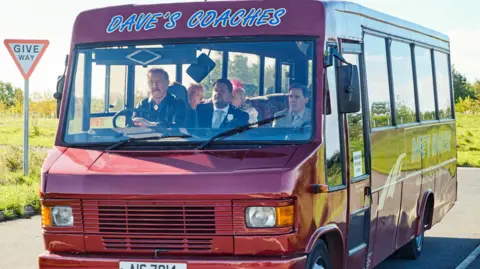 BBC/Toffee International Ltd/Tom Jackson A still from Gavin and Stacey showing actor Steffan Rhodri driving the Dave's Coaches bus, with Rob Brydon, James Corden, Larry Lamb and Alison Steadman as passengers.