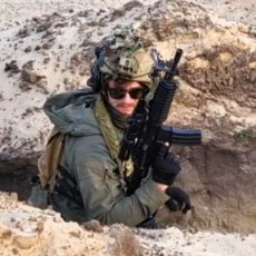 A man in combat uniform standing in a trench, holding a gun and looking on