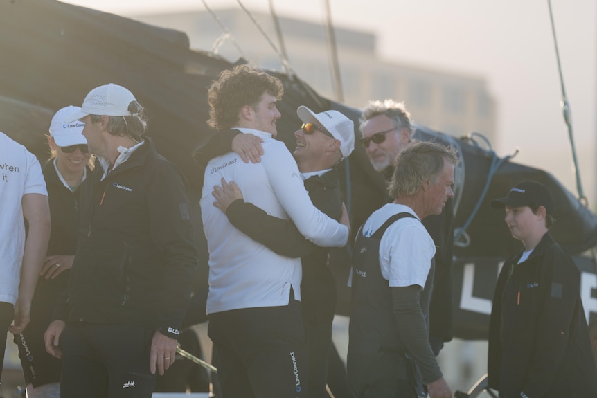 Crew members hug on board a sailing boat.