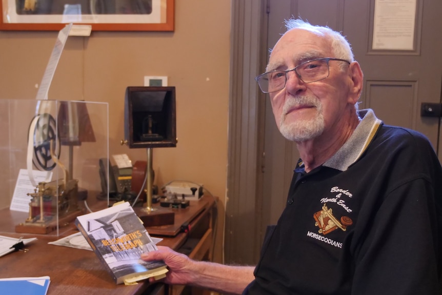 A man holding a book sitting in front of old Morse code equipment