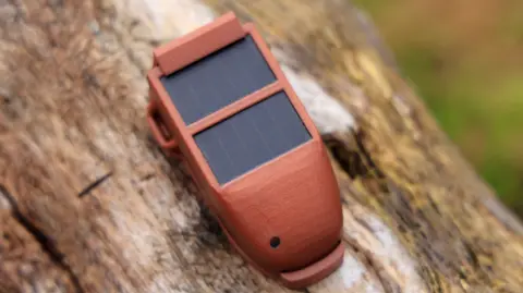 Nick Whittle A brown satellite tracking device, with small solar panels, placed on a log