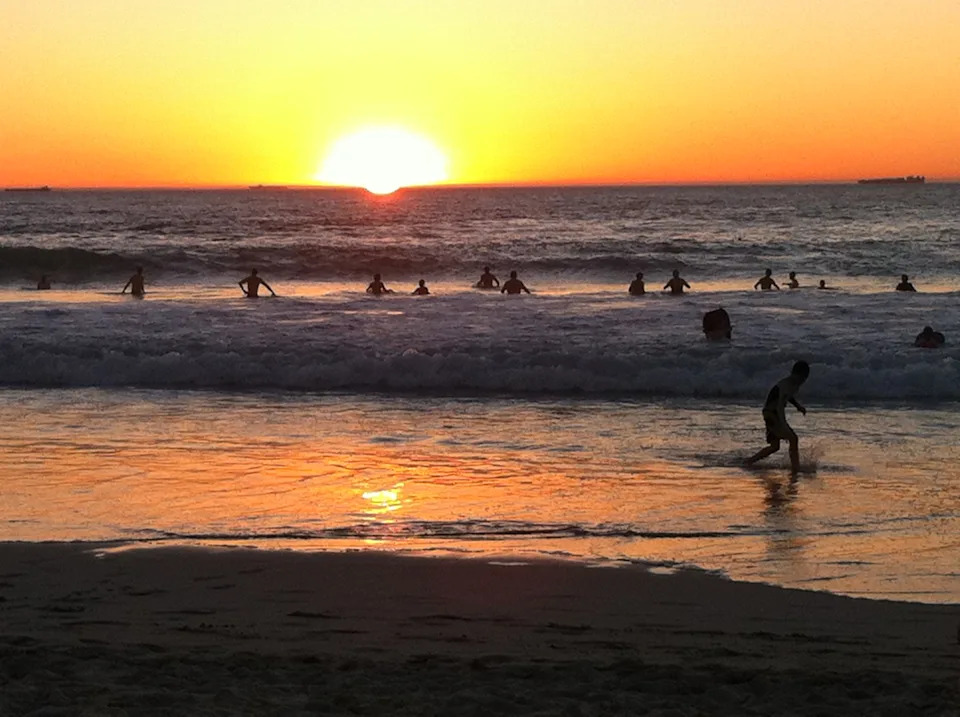 Swimmers relaxing late evening at Trigg Beach Western Australia, as the sun sets during a heatwave.