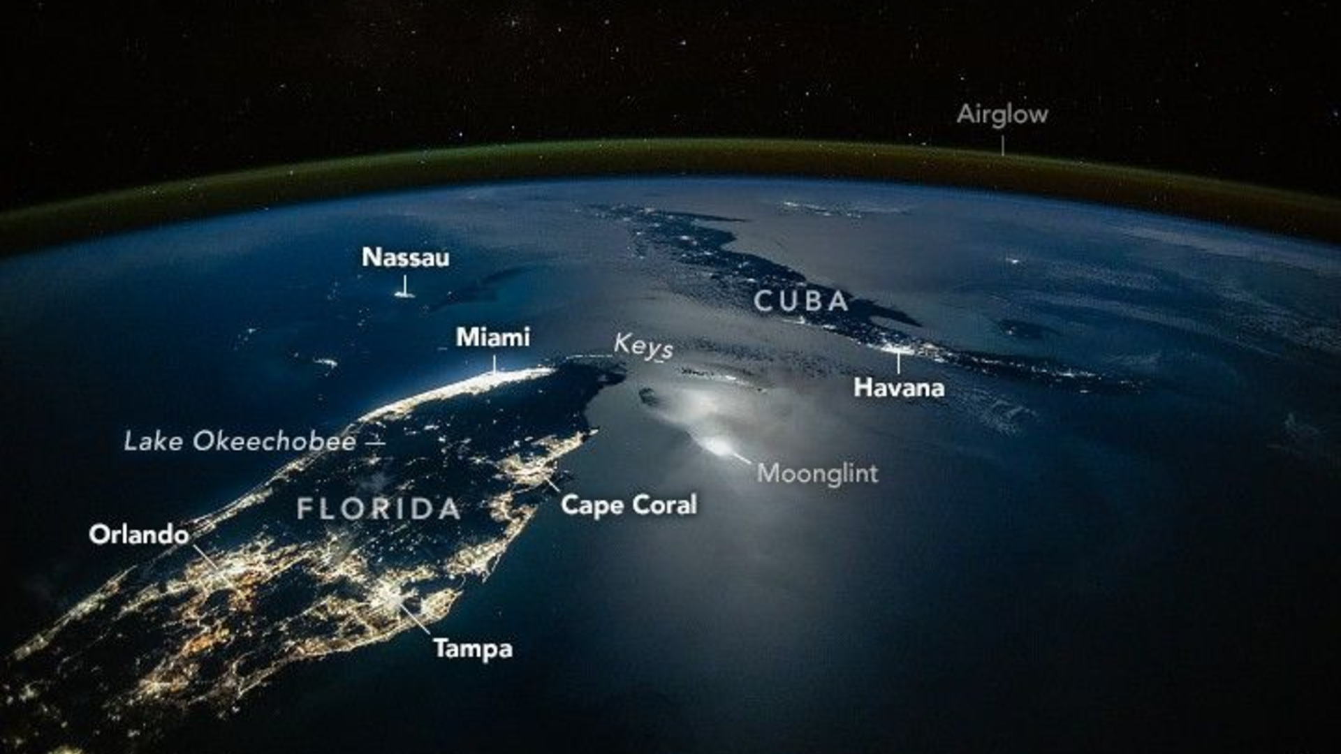 A photograph of the tip of Florida and nearby Cuba from space, with lights from cities illuminating the surface of the planet, labeled cities like Orlando and Tampa are seen as well as a green surface over Earth's labeled airglow