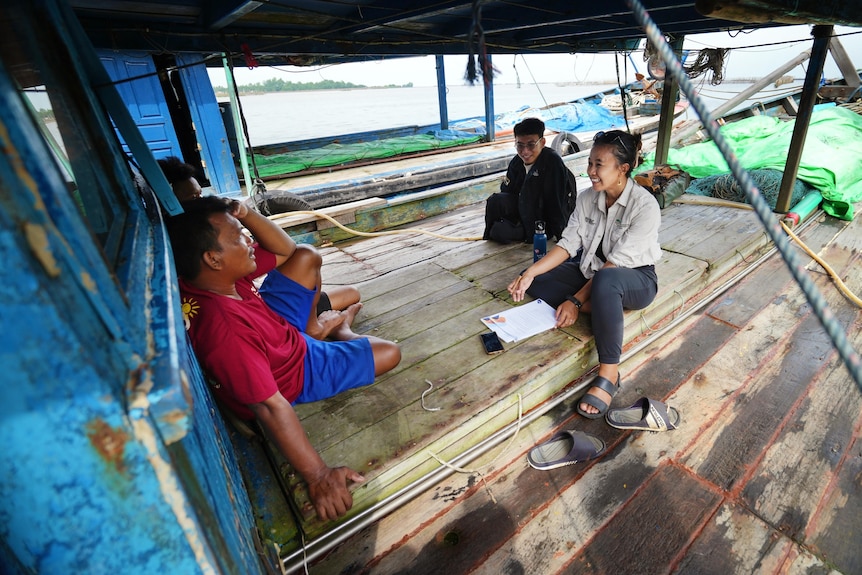A person on an Indonesian fishing boat has a recorder and notebook as she talks to a fisherman.