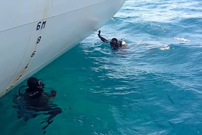 Two divers at the surface of turquoise water at the hull of a ship.