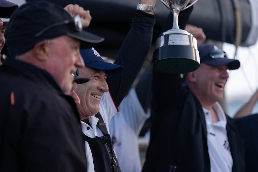 A man holds a big trophy with his arms raised