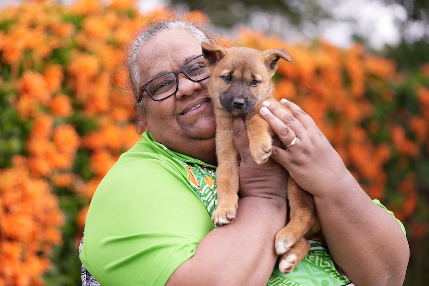 A smiling Aboriginal woman cuddles a dingo pup.