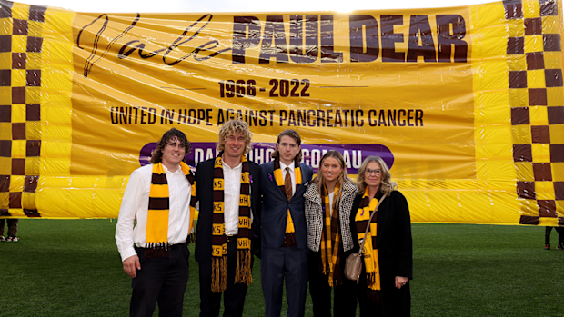The family of late Paul Dear pose for a photo in front of the Hawks' banner ahead of their round 18 match in 2022.