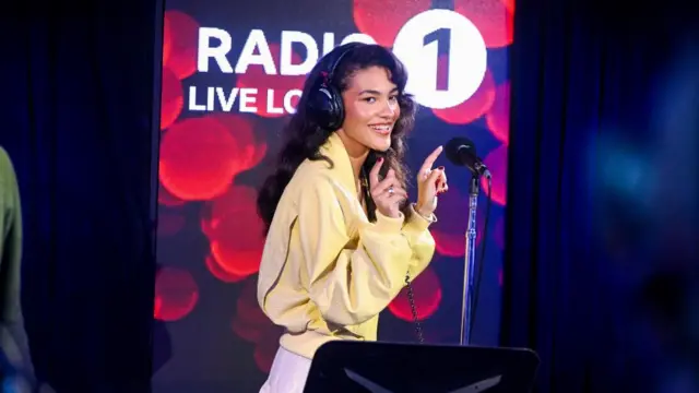 Olivia Dean performing on Radio 1's live lounge. She is wearing a yellow jacket