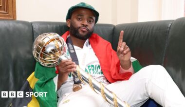 South Africa captain Temba Bavuma, draped in a flag, holds up one finger as he celebrates winning the World Test Championship final