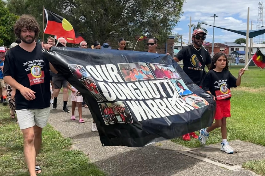 People march with banner and Aboriginal flag