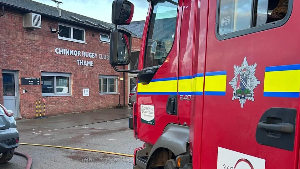 A fire engine next to one of the entrances of the rugby club, a two-storey red brick building.