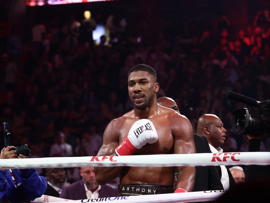 Boxer Anthony Joshua sands in the ring holding his glove to his chest in acknowledgement of the crowd.