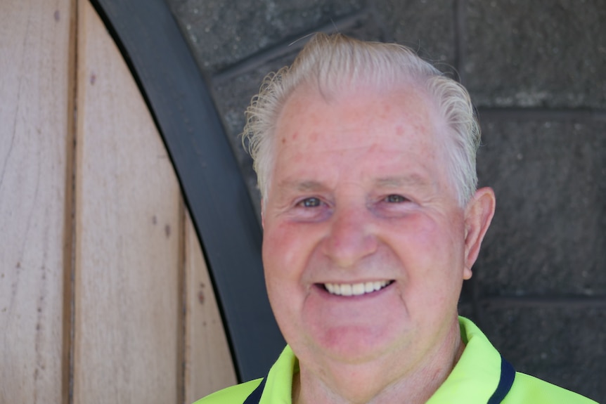 A smiling man with grey hair wearing a high-vis shirt.