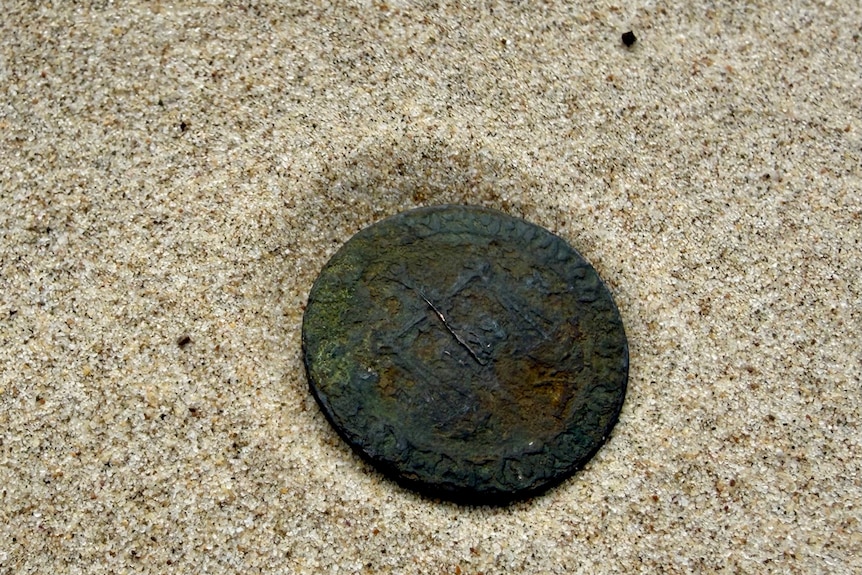 A very old worn copper coin sitting on the sand.