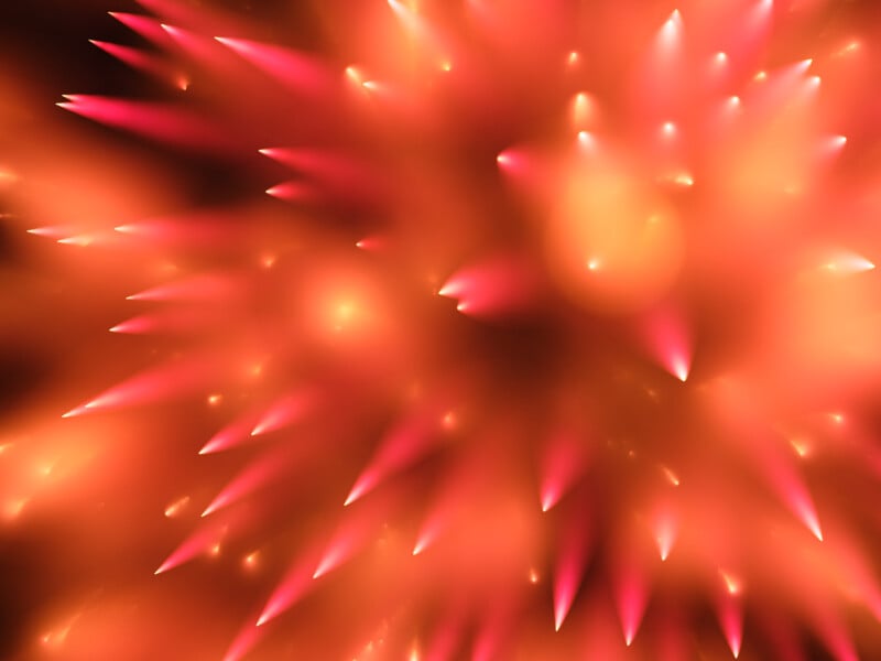 Bright, abstract image featuring glowing red and orange spikes radiating outward, creating a dynamic burst of light with a soft, blurred effect in the background.