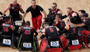Canadian wheelchair rugby players form a circle on court. A male coach is speaking