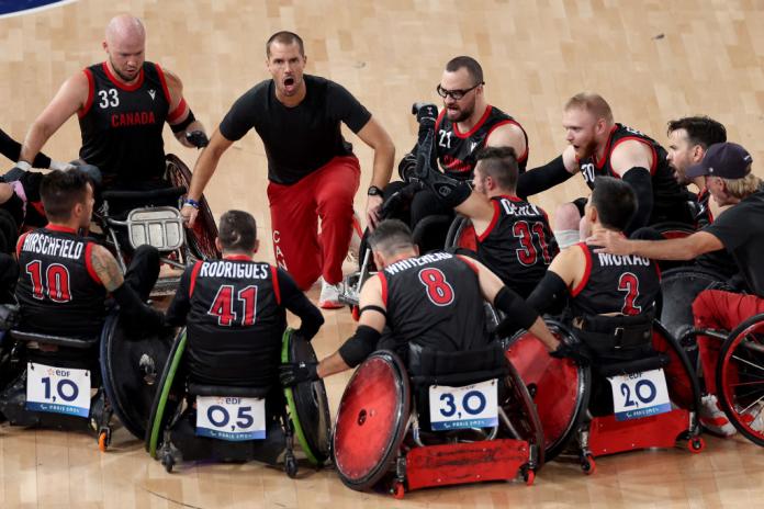 Canadian wheelchair rugby players form a circle on court. A male coach is speaking