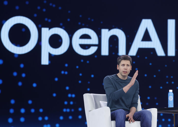 Speaker in a chair presenting on stage with OpenAI logo behind, discussing AI industry dirty secrets and insights.