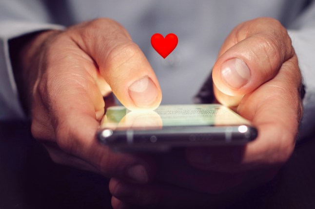 An adult man's hands typing on a smartphone with a heart emoji above it.