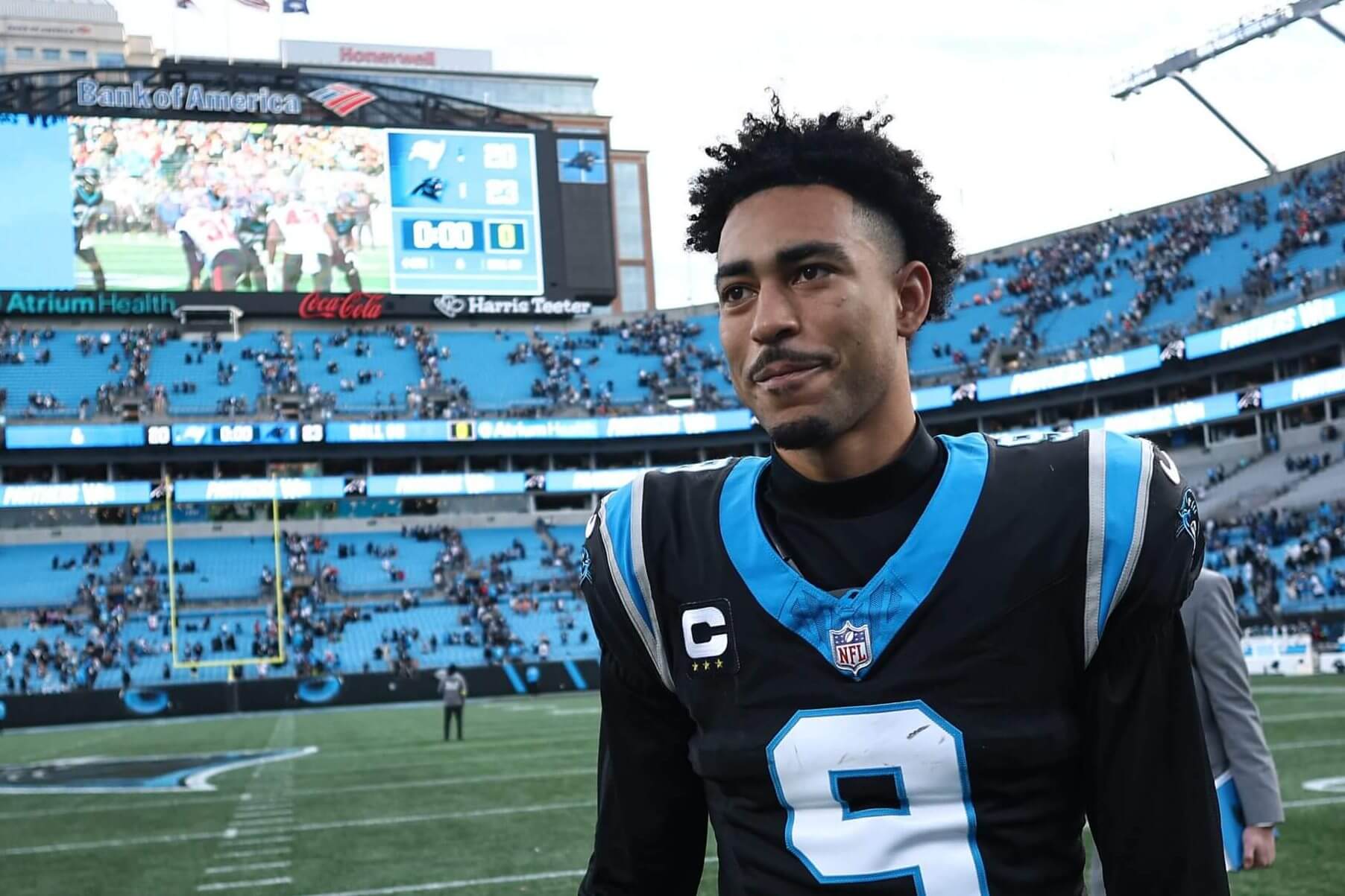 Bryce Young, wearing a black No. 9 uniform and no helmet, smiles and looks ahead while walking off the field.