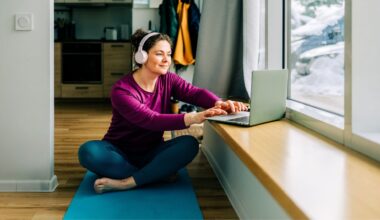 Woman setting up laptop to do low-impact cardio workout at home on yoga mat with snow outside window and wearing headphones