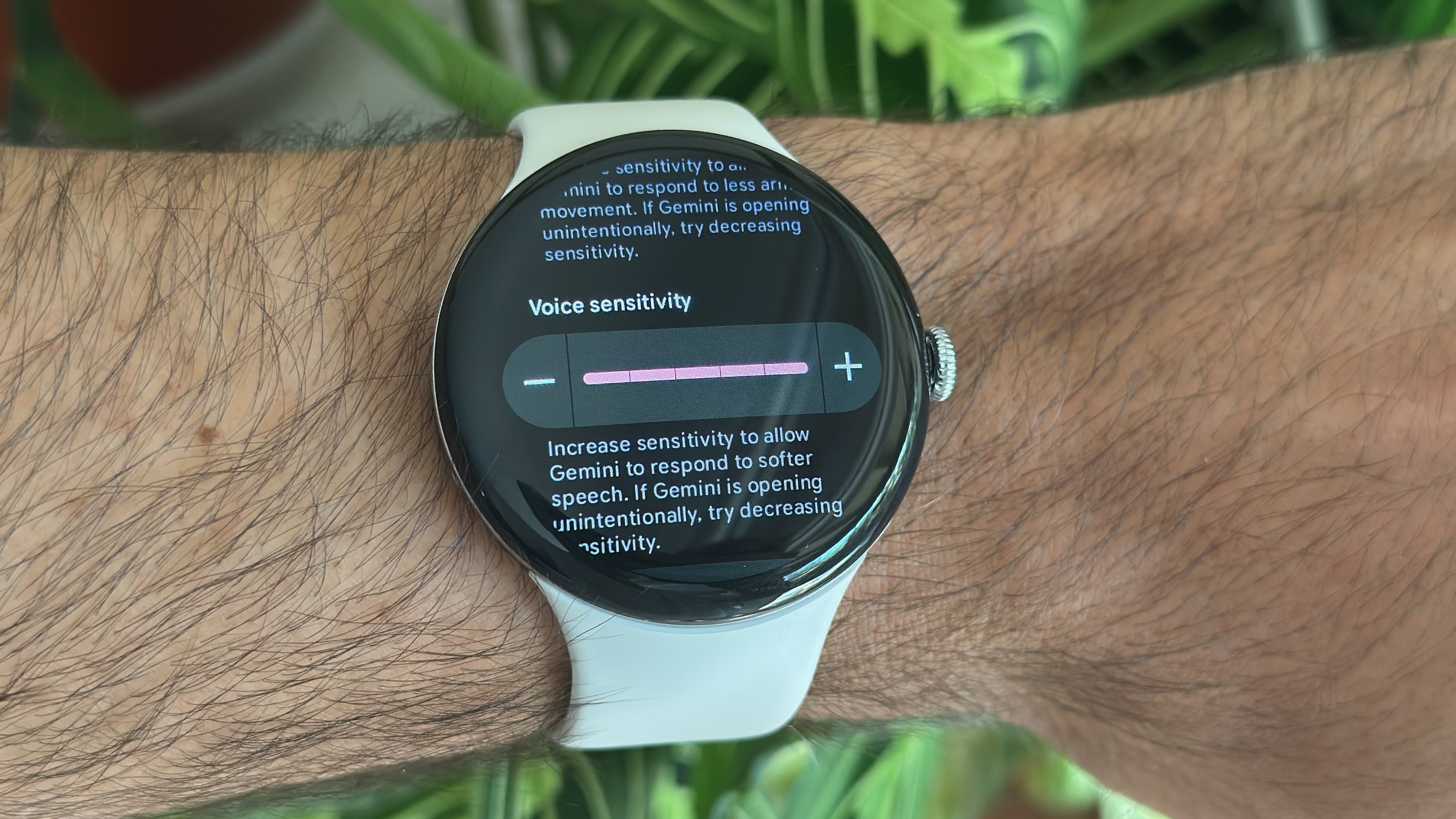 A photo of the Google Pixel Watch 4 on a man's wrist, showing the Voice sensitivity setting set to 5/5 for the Gemini Raise to Talk feature.