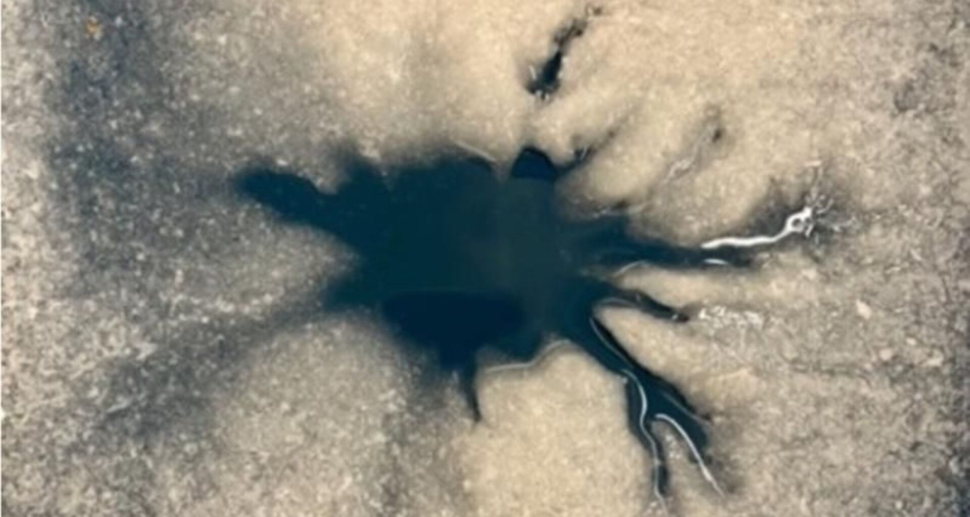 A dendritic shaped dark spot is seen against an icy surface