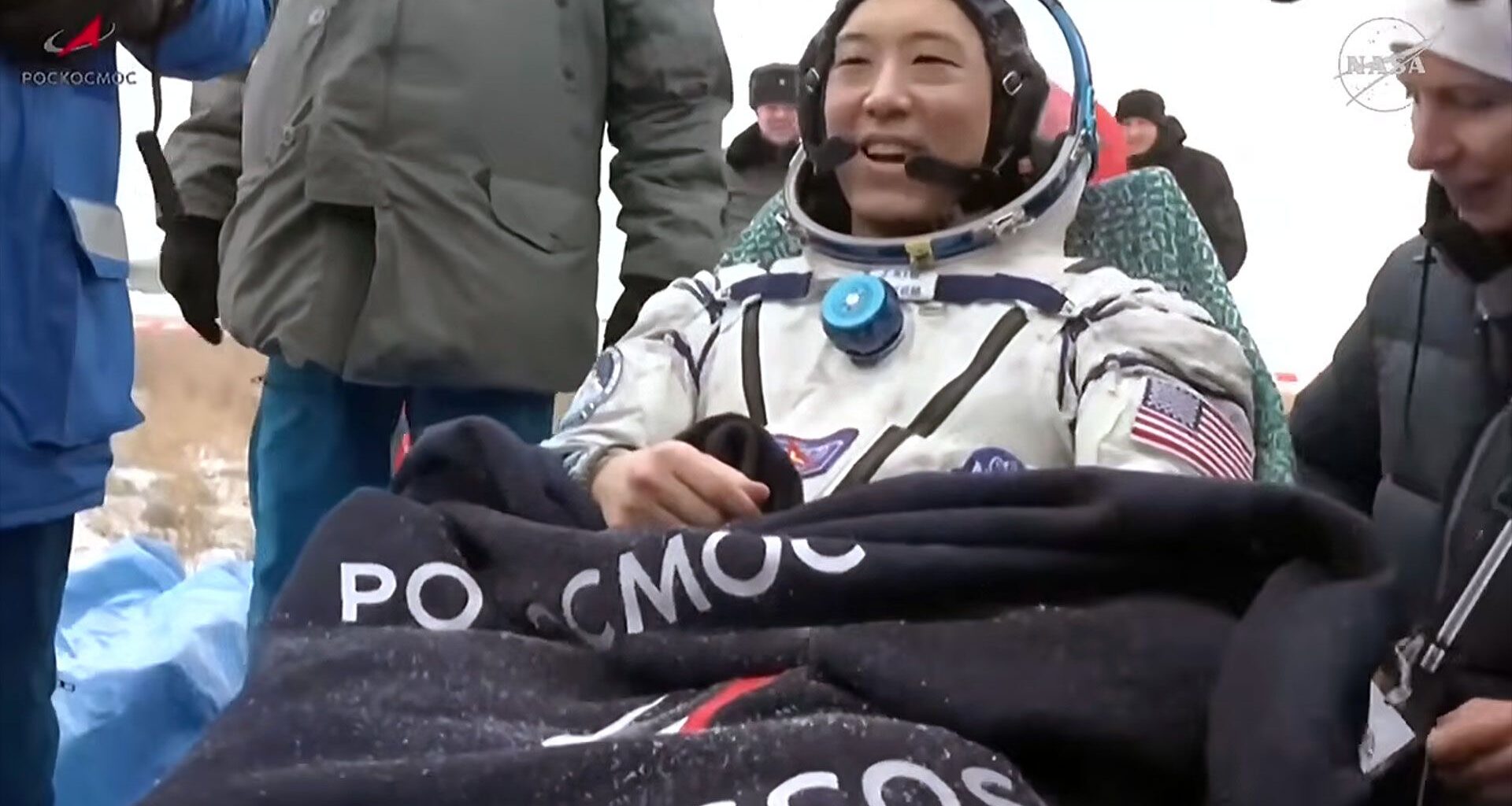 a man in a white pressure suit sits outside his spacecraft after landing back on Earth