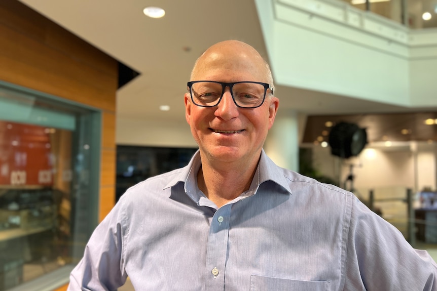 A man in a blue business shirt smiles with hands on hips