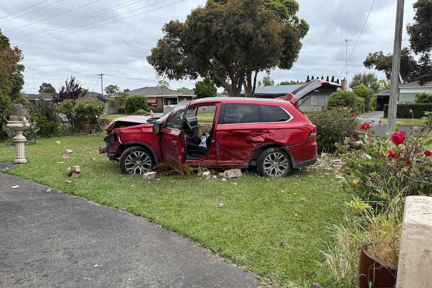 Damaged red SUV on grass, bricks on the ground