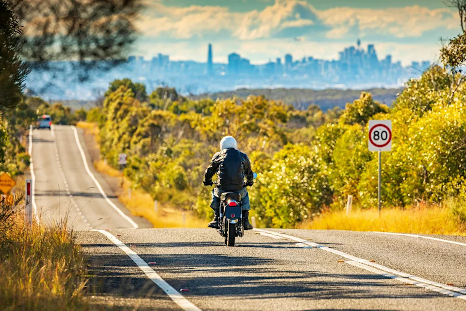 View across Royal National Park toward Sydney city on horizon, man rides motorbike.