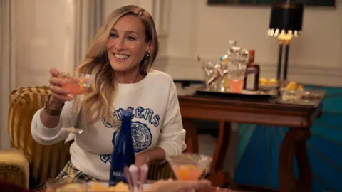 Warner Brothers Discovery Sarah Jessica Parker holds up a glass in a scene from Sex and the City 