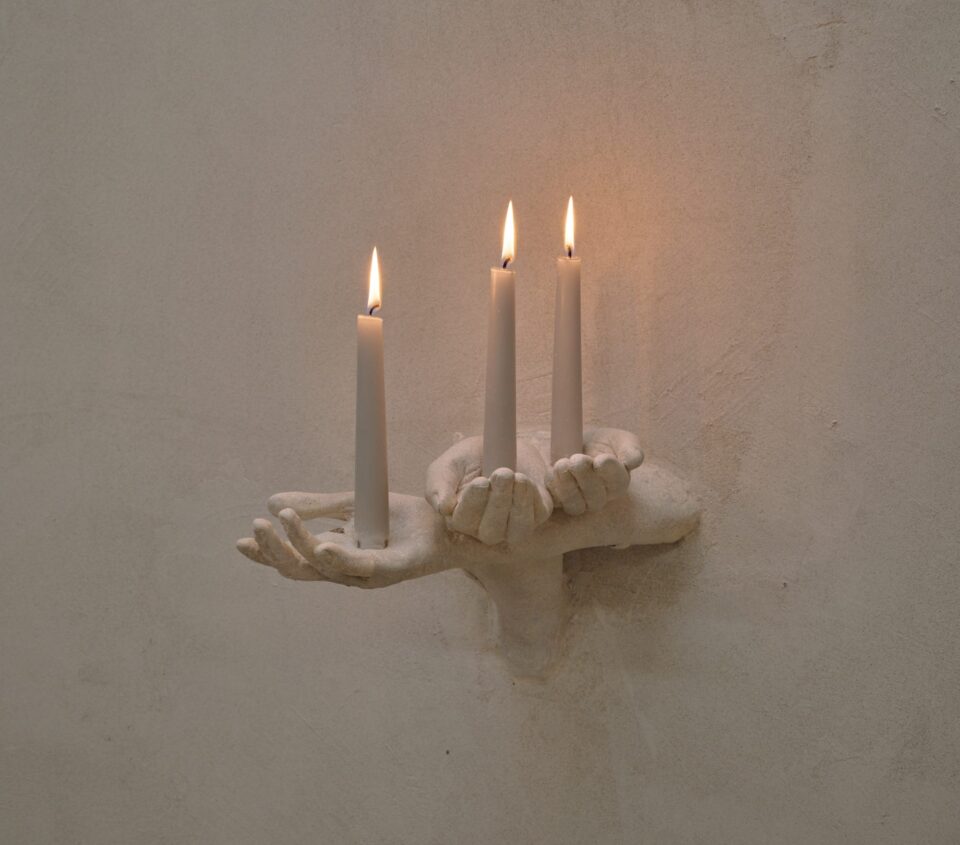 An art installation by Clementine Keith-Roach and Christopher Page of plaster-cast hands holding three candles like a wall sconce