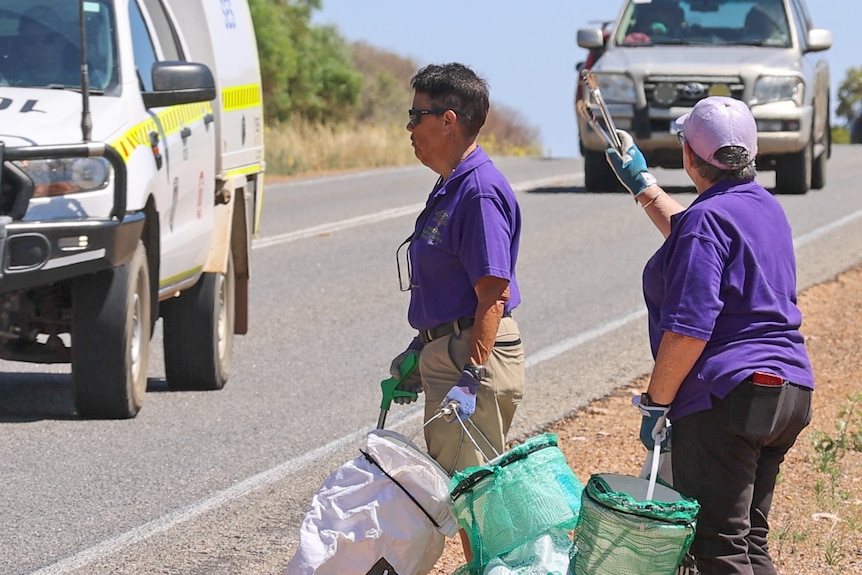 Glenda Green waves to cars from the side of the road.