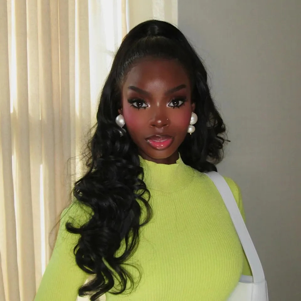 person wearing a bright yellow sweater with pearl earrings and a white handbag