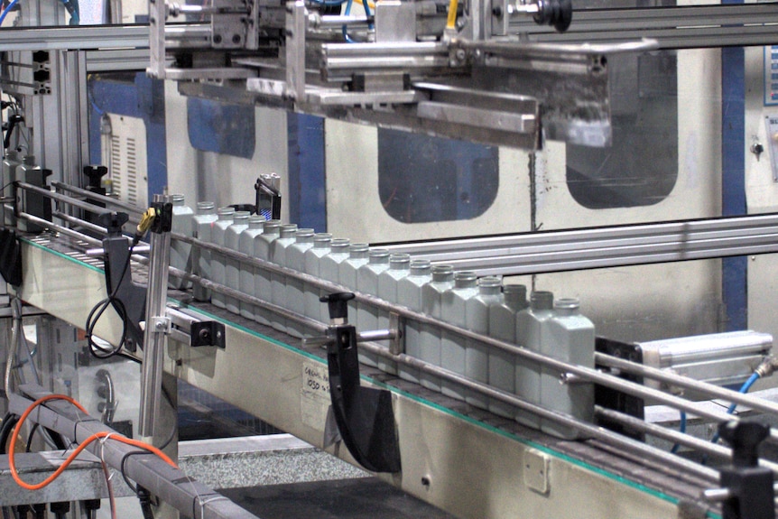 A row of grey plastic bottles on a factory conveyer belt.