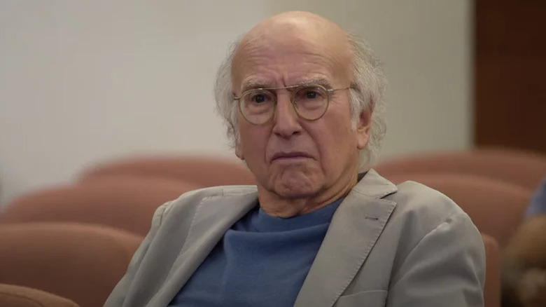 Larry David sits with a disgruntled look on his face on Curb Your Enthusiasm