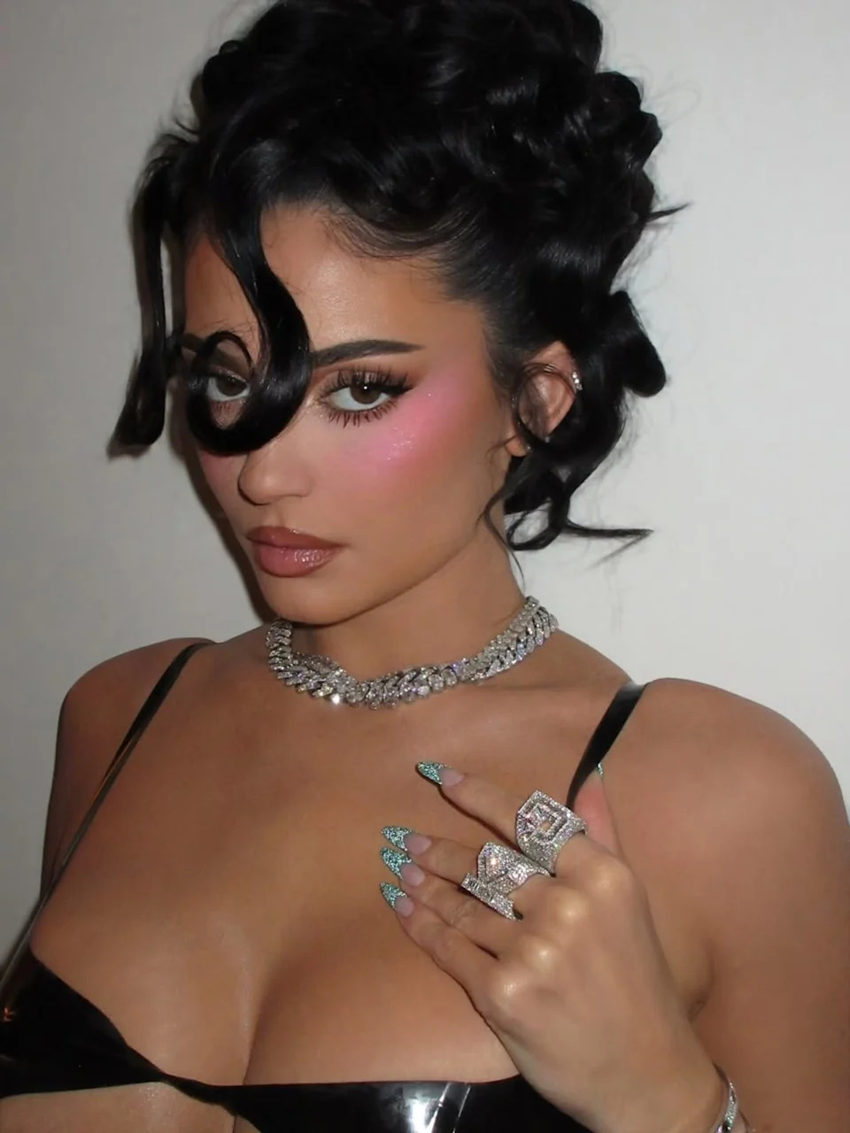 person wearing a shiny black outfit adorned with jewelry and elaborate nail art