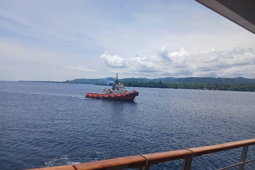An orange tugboat on the water, with forested land in the background.
