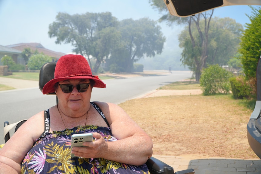 A lady in a wheelchair checks her phone on a smoky street