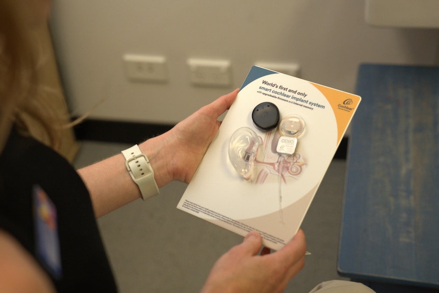 A woman holds a CI in packaging that reads: "World's first and only smart cochlear implant system".