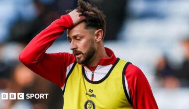 Harry Cornick runs his hand through his hair, dressed in a red training top and a yellow bib