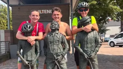 Handout The three young men are standing behind three statues, which are peeing into a fountain.