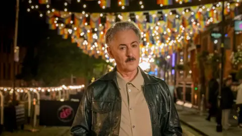 Quay Street/ITV Productions/Channel Four Alan Cumming dressed in shirt and leather jacket looking at the camera