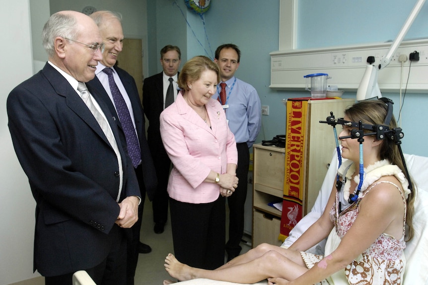 A man stands next to a woman speaking to another woman who is wearing a neck and head brace