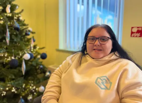 A girl in glasses sat next to a Christmas tree
